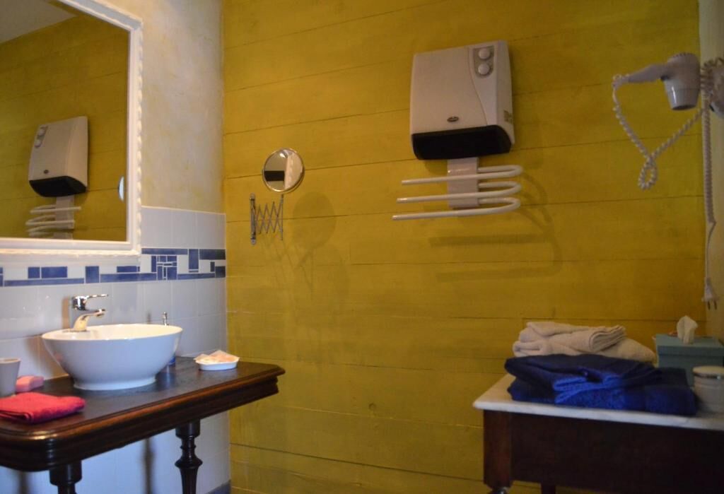 Un baño con pared amarilla, lavamanos blanco, espejo, toallero y secador de pelo.