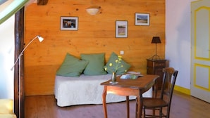Een knus interieur met een houten wand, een bed met groene kussens, een tafeltje met een vaas en een lamp.