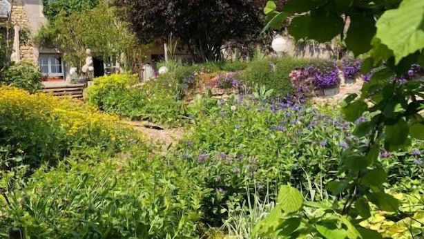 Een huis met een rood pannendak, omgeven door een tuin met diverse planten en bloemen.