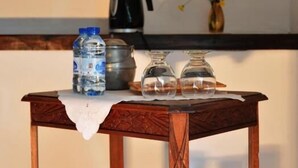 Een houten tafel met een wit kleed, waterflessen, een koffiepot en een vaas met gele bloemen.