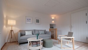 En moderne stue med en grå sofa, et rundt bord, en træstol og en lampe.