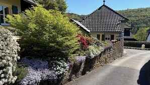 En traditionel bygning med et tag af teglsten, omgivet af frodigt grønt og blomstrende planter.