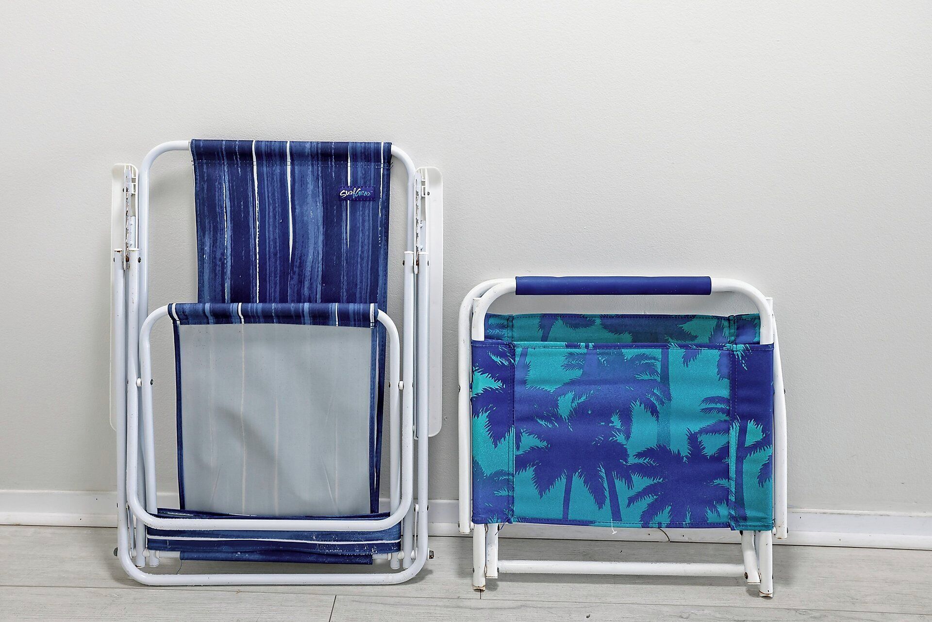 Two portable chairs with different fabric designs, one with a striped pattern and the other with a palm tree print, against a plain wall.