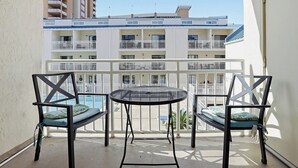 A balcony with two chairs and a table, overlooking a building with multiple balconies. - OceanView Studio Condo in Orange Beach | 4 Pools (Orange Beach, AL)