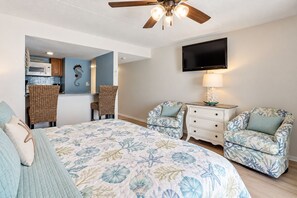 A bedroom with a bed, two chairs, a nightstand, a television, and a ceiling fan.