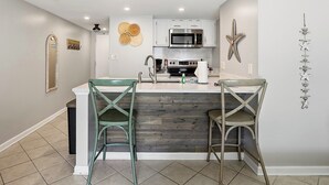 A kitchen with a central island, two bar stools, a microwave, and a sink. - OceanView Studio in Orange Beach | 4 Pools (Orange Beach, AL)