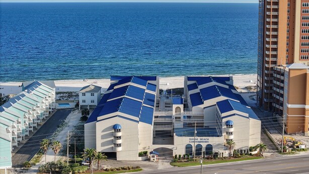 A coastal building with a modern design, featuring a prominent blue roof and a view of the ocean. - OceanView Studio in Orange Beach | 4 Pools (Orange Beach, AL)