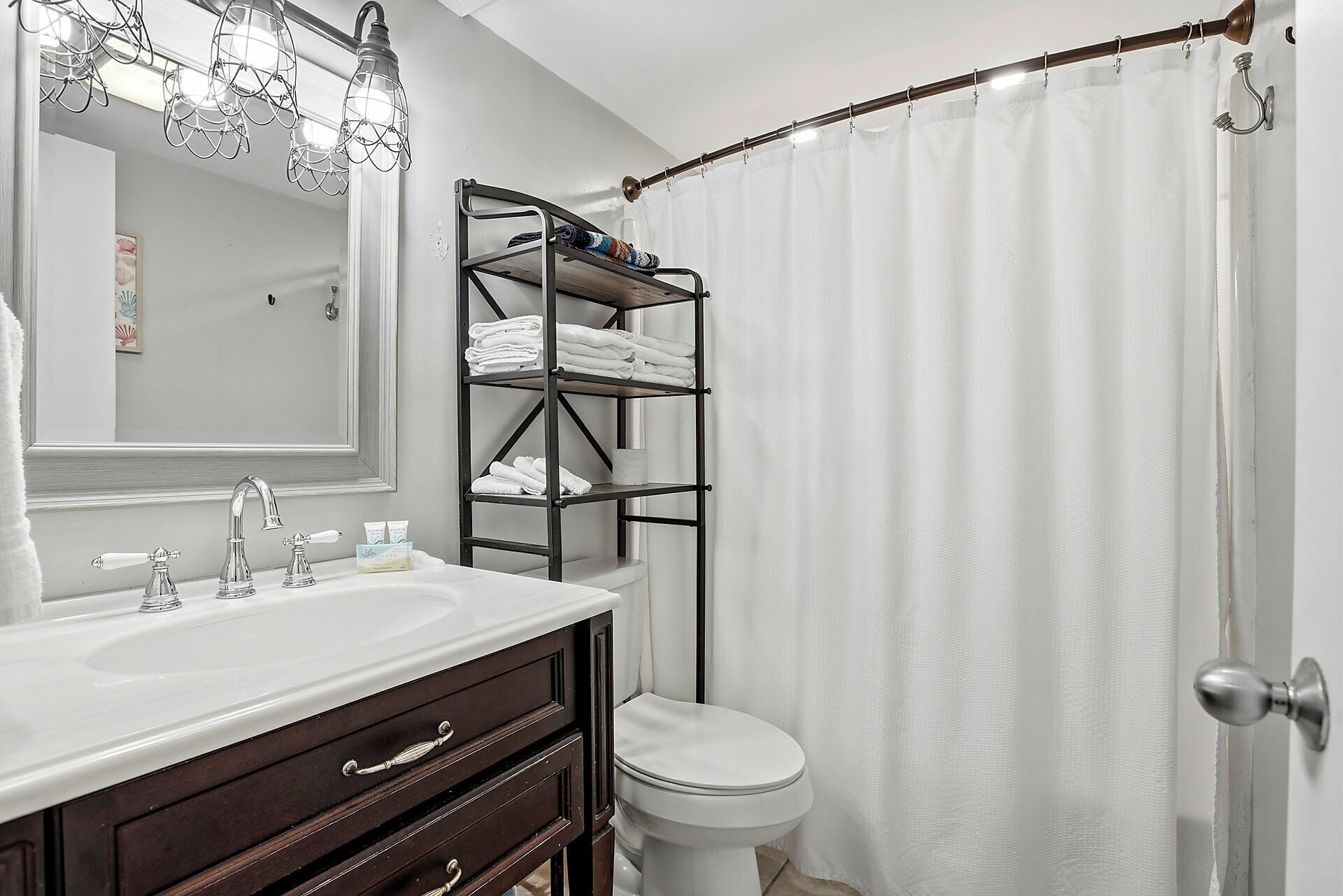 Een badkamer met een witte wastafel, meubel en toilet. Er is een handdoekhouder met opgevouwen handdoeken en een douchegordijn.