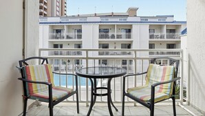 A balcony with two chairs and a table, overlooking a building with multiple balconies. - OceanView Studio in Orange Beach | 4 Pools (Orange Beach, AL)