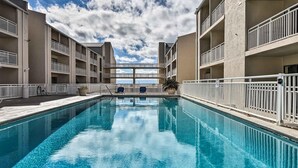A swimming pool with clear blue water, surrounded by a white fence and a building with multiple balconies. - OceanView Studio in Orange Beach | 4 Pools (Orange Beach, AL)