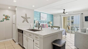 A modern kitchen with a central island, a built-in dishwasher, and a large window overlooking a balcony. - OceanView Studio in Orange Beach | 4 Pools (Orange Beach, AL)