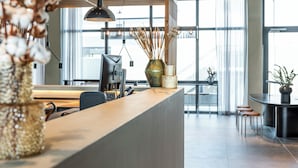 A modern reception desk with a computer, a vase with dried plants, and a large window with a view of the city. - Zleep Hotel Hamburg Volkspark (Hamburg)