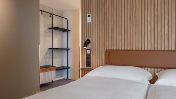 Ein Hotelzimmer mit zwei Betten, einem Holzkopfende, einem Kleiderschrank mit Regalen und einem Nachttisch mit Lampe.