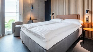 A modern hotel room with a large bed, a small round table, a chair, and a view of the outdoors. - Zleep Hotel Hamburg Volkspark (Hamburg)