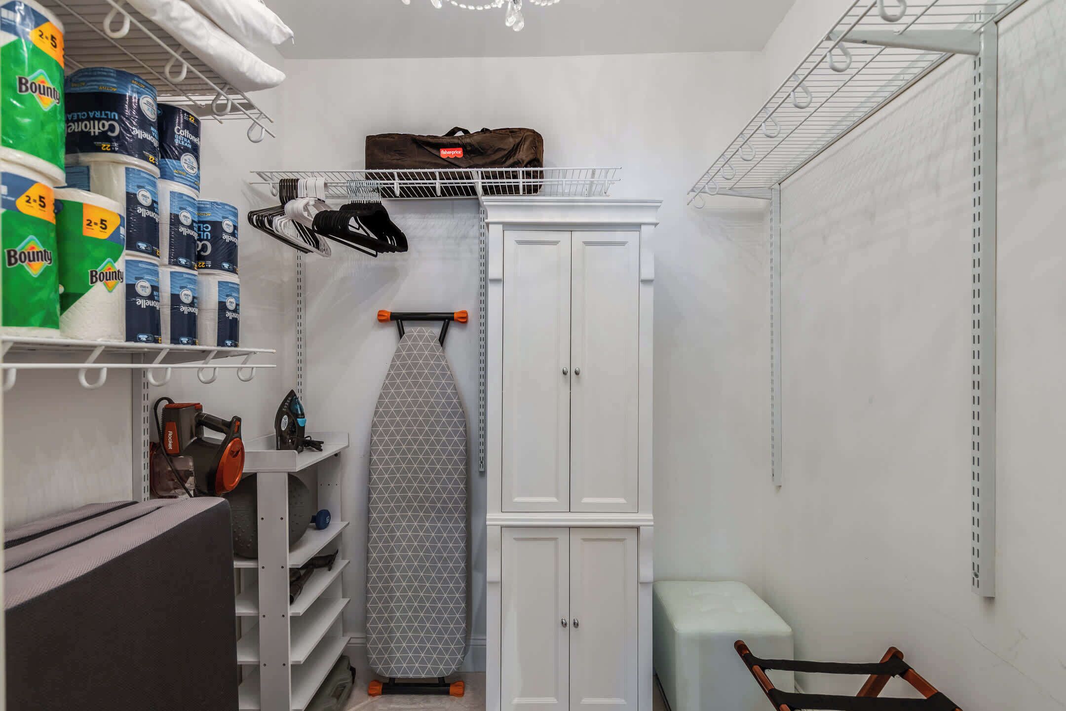 A laundry room with shelves of Bounty toilet paper, a hanging iron, and a storage cabinet.