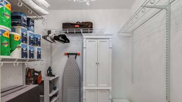 A laundry room with shelves of Bounty toilet paper, a hanging iron, and a storage cabinet.