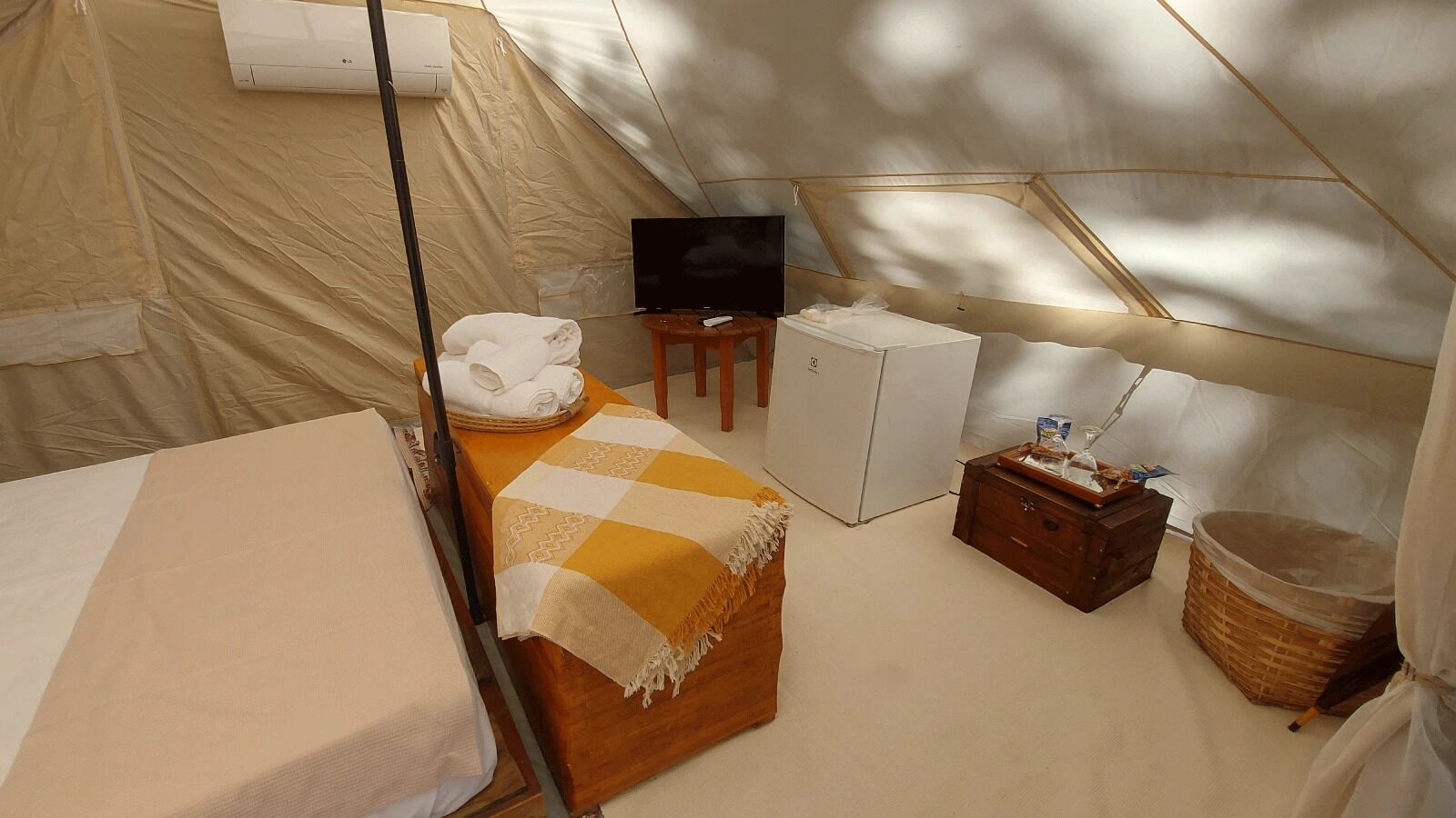 Een tentaccomodatie met een bed, een televisie, een kleine koelkast en een houten kast.