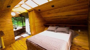 Un dormitorio de cabaña de madera con cama, ventana y tragaluz.