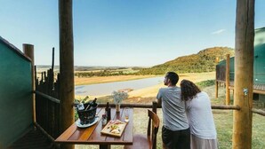 Una pareja cenando en una mesa de madera con vista a un río y colinas.