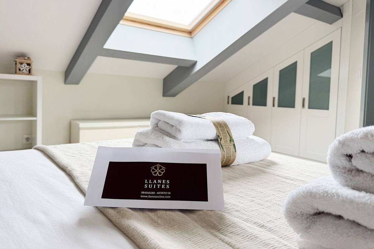 Una habitación de hotel con tragaluz, toallas ordenadamente dobladas, una cama y una tarjeta de presentación sobre la cama.