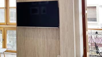 Una stanza con una grande TV a schermo piatto montata su un parete in legno, una finestra che offre vista sull'esterno e una porta che dà su una zona all'aperto.