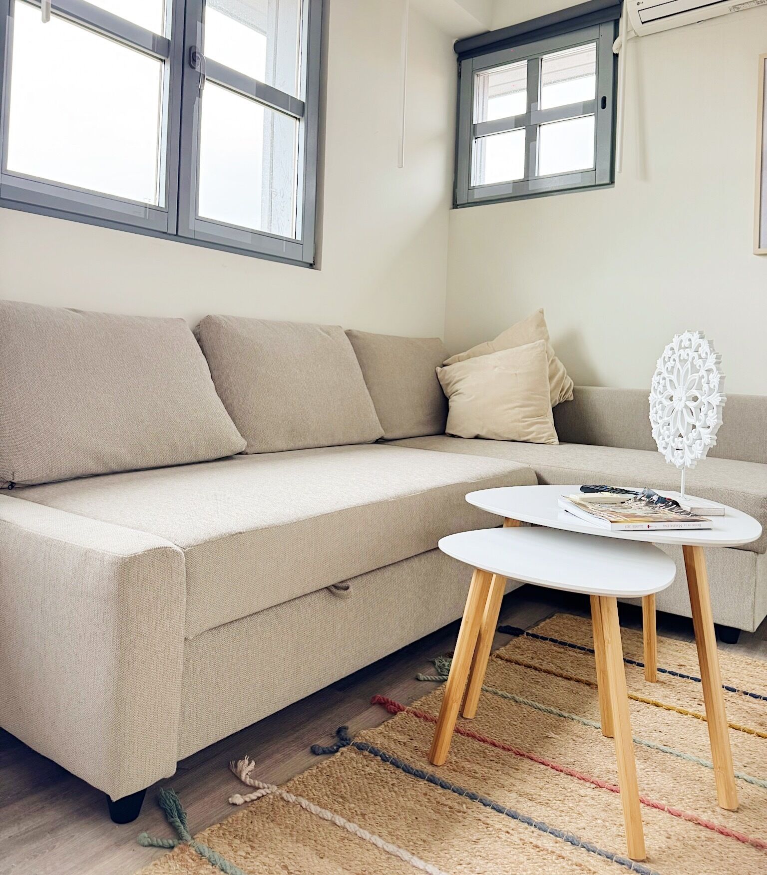 A modern living room with a beige sectional sofa, a white round coffee table, and a colorful woven rug.