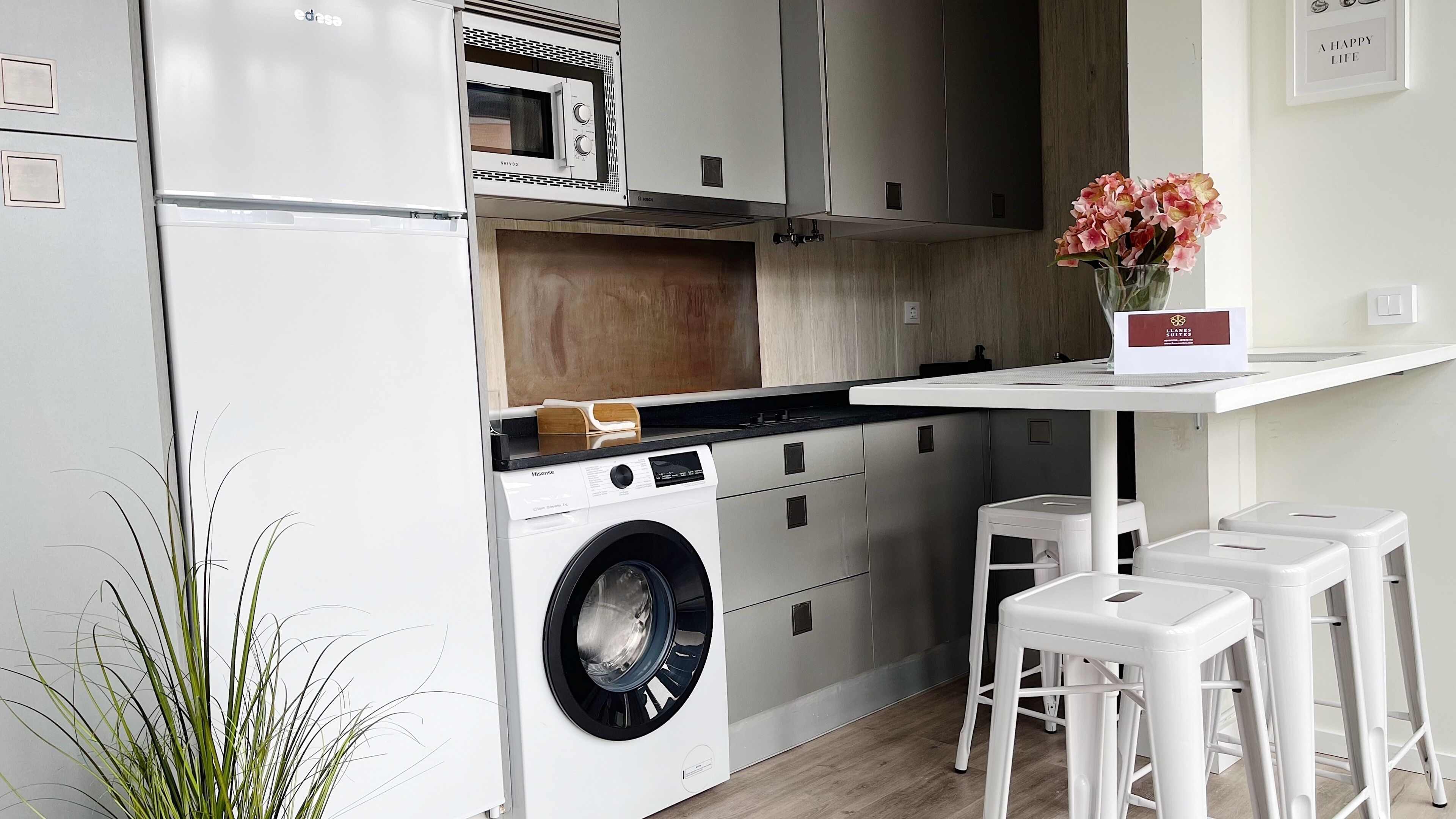Une cuisine compacte équipée d’un lave-linge, d’un four à micro-ondes et d’un petit coin repas avec des tabourets.