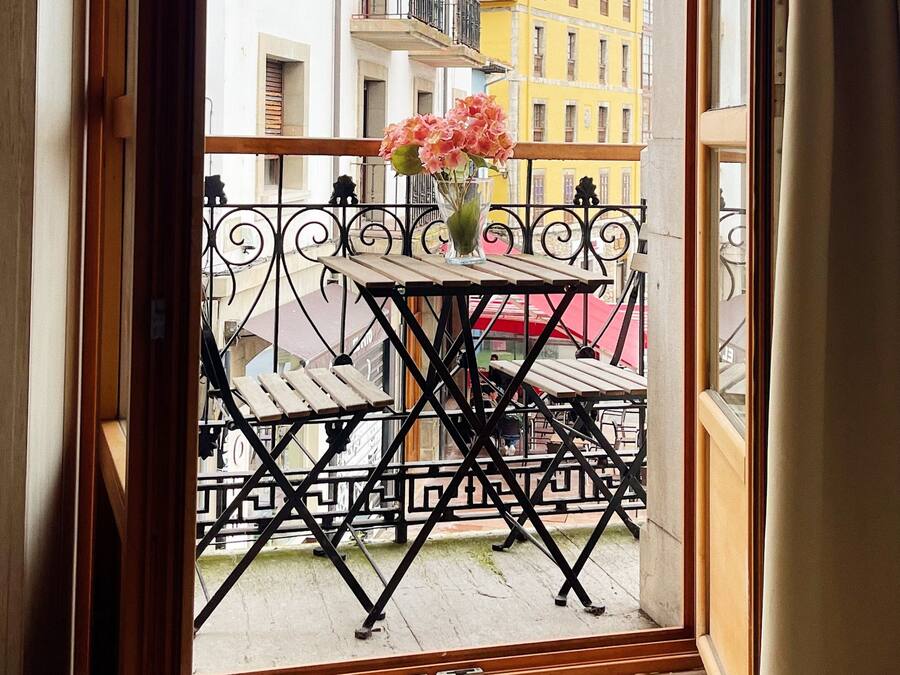 Un balcón con mesa y sillas, un florero con flores y vistas a edificios.