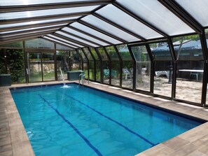A swimming pool with a glass enclosure, clear water, and a view of the outdoors.
