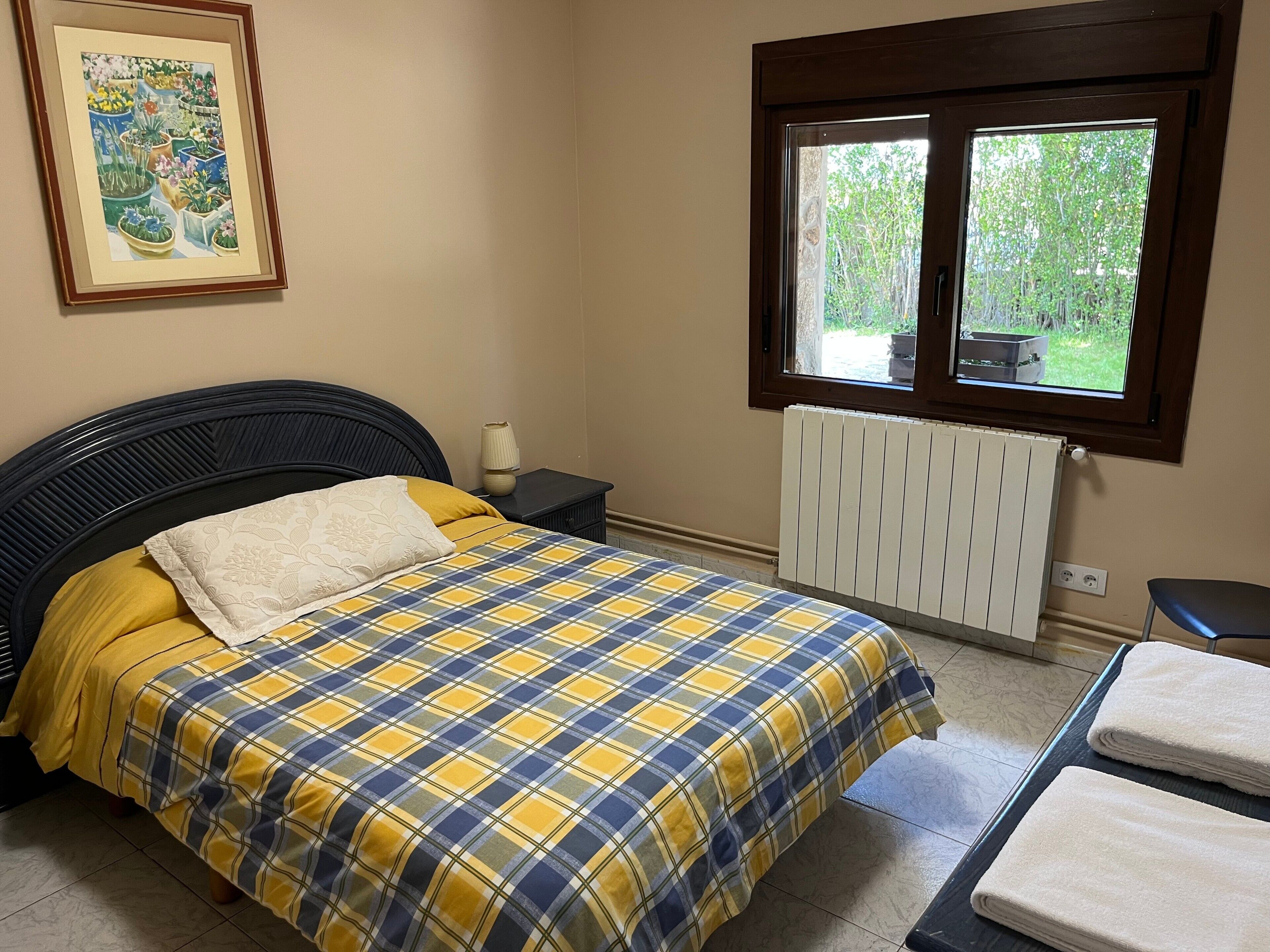 Een slaapkamer met een bed, nachtkastje, raam, radiator en een lijst aan de muur.