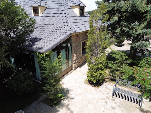A stone building with a tiled roof, a stone pathway, and various green shrubs.