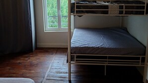 Quarto com beliche, janela com vista para vegetação, piso de madeira e luminária pendente.