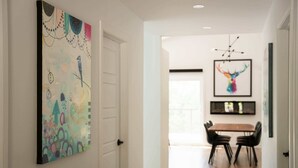 Un pasillo con comedor, que presenta un cuadro abstracto de gran tamaño, una obra de arte colorida en la pared y una lámpara de araña moderna.