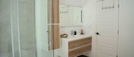 Un baño moderno con cabina de ducha de vidrio, tocador de madera y una puerta blanca con perchero.