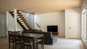 Un salón amplio con una escalera de madera, una mesa de comedor con sillas, un sofá gris y un televisor.