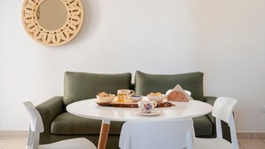 A round dining table with a white tablecloth, surrounded by white chairs, set with breakfast items and a decorative mirror on the wall.