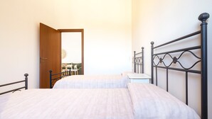 A bedroom with two beds, a wooden door, and a view of a dining area.