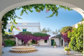 Une cour avec une fontaine, des plantes en pot et un bâtiment doté d’un balcon.