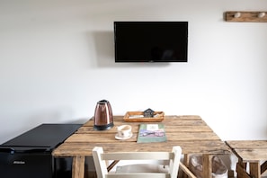 A room with a wooden table, a black coffee maker, a cup, a tray with snacks, a magazine, a TV mounted on the wall, and a black refrigerator. - Room 'San Biagio - Deluxe 2' with Shared Pool, Wi-Fi and Air Conditioning (Calimera)