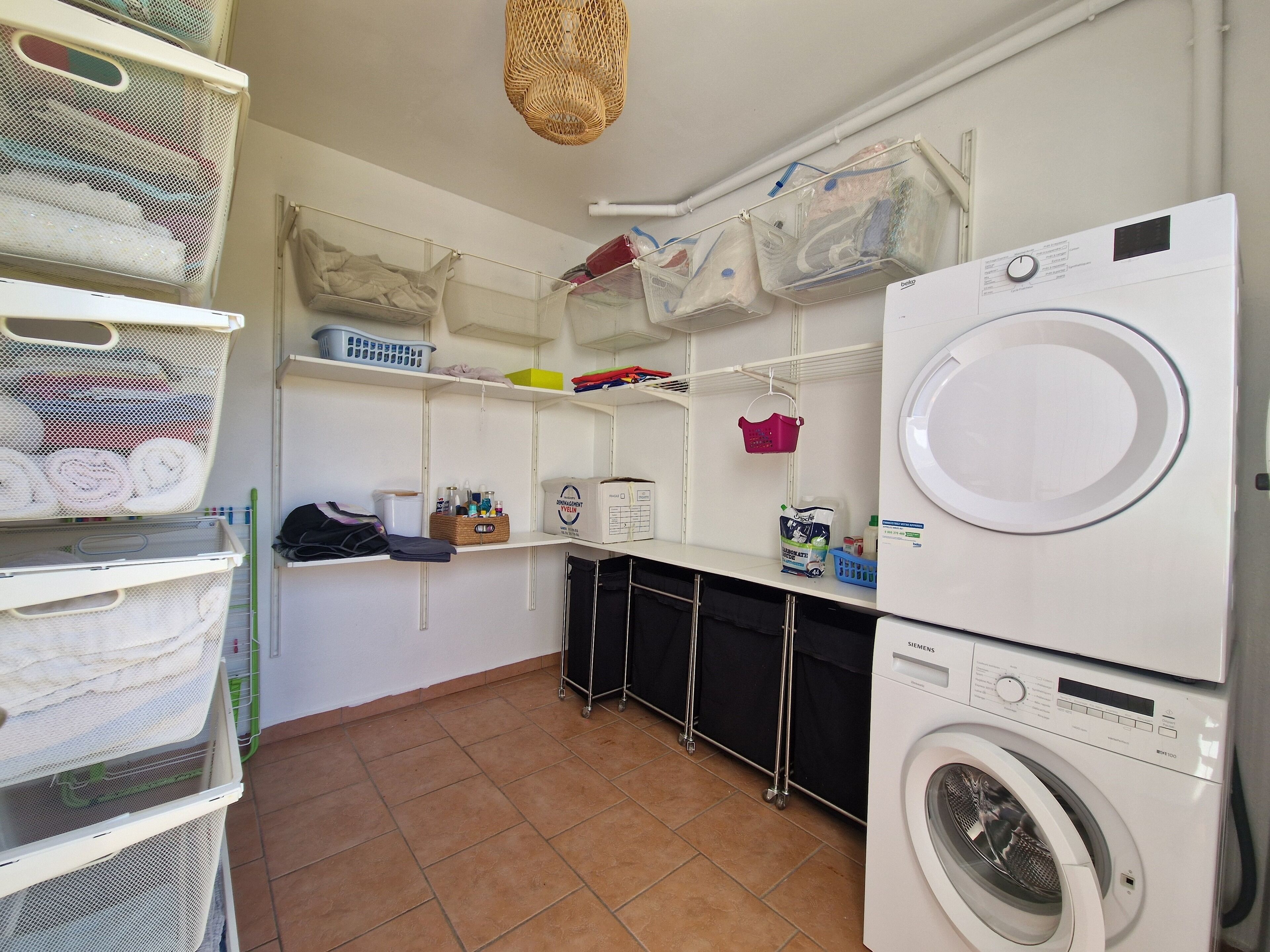 A laundry room with a front-loading washing machine, shelves with folded towels, baskets, and cleaning supplies.