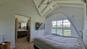 A bedroom with a canopy bed, a bathroom with a mirror and sink, and a view of greenery outside.