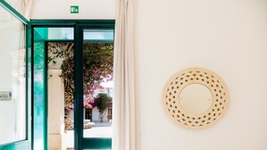 An open door leading to a courtyard with a pool, a wall-mounted decorative mirror, and a green-framed door.