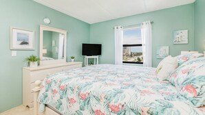 Ein Schlafzimmer mit geblümtem Bettbezug, einem Schminktisch, einem Fernseher, einem Fenster mit Vorhängen und Bildern an den Wänden.