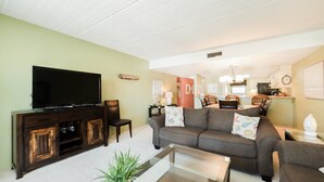 Ein Wohnzimmer mit Flachbildfernseher, dunklem Medienmöbel und grauem Sofa mit gemusterten Kissen.