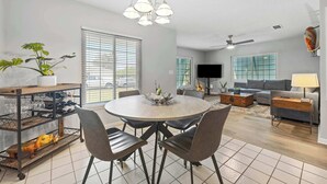 Un salon moderne avec une table à manger ronde, des canapés gris, un téléviseur et un ventilateur de plafond.