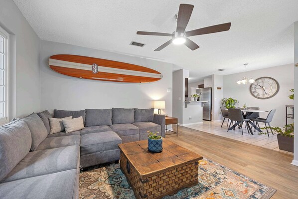 A modern living room with a sectional sofa, a wooden coffee table, and a surfboard on the wall. - Casa Playa Private Home for 6! (St. Augustine)