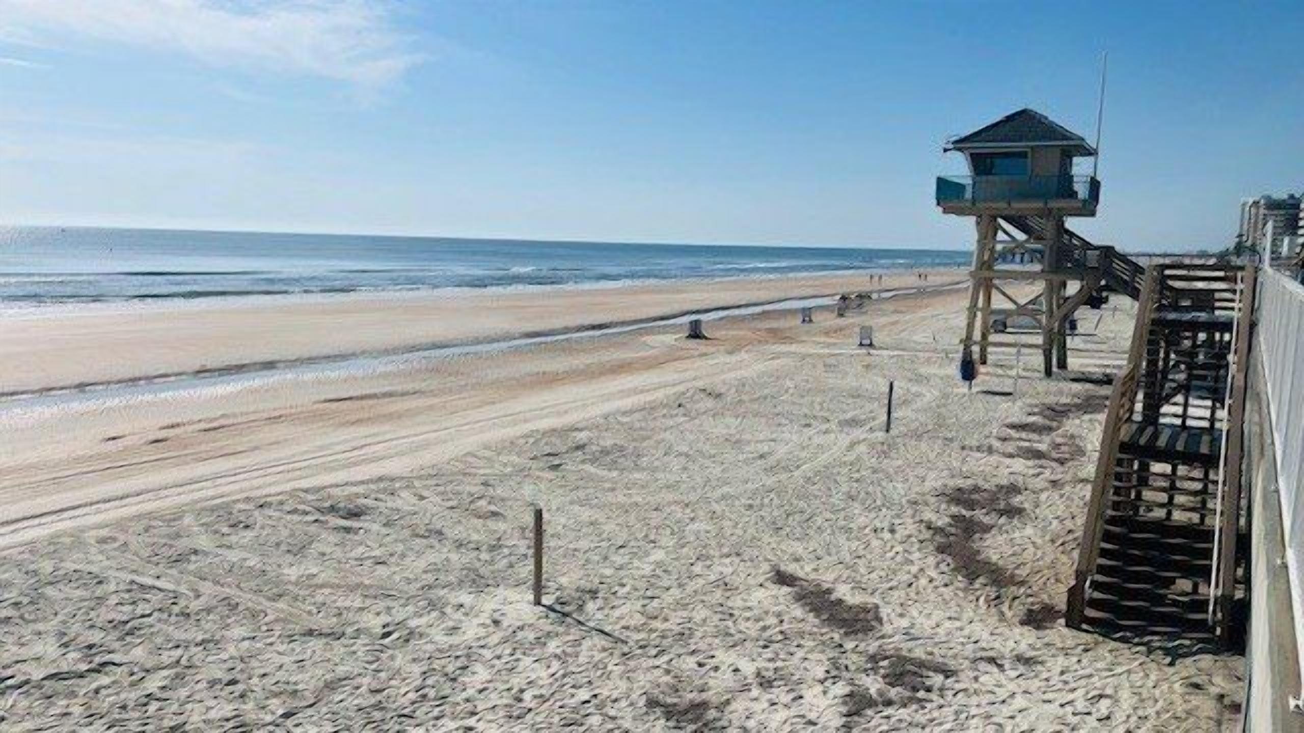 A beach with a lifeguard tower and a wooden structure with steps.