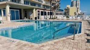 Una piscina con bordo piastrellato, lettini prendisole e un edificio con balconi sullo sfondo.