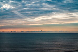 A coastal view with a calm sea and a distant city skyline under a cloudy sky.
