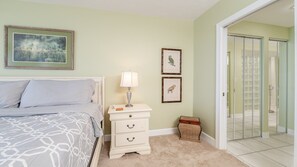 A bedroom with a bed, bedside table, lamp, framed pictures, and a door leading to a bathroom.